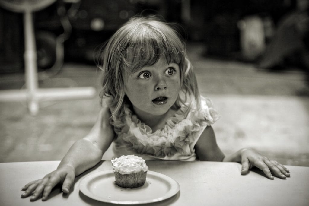 Une petite fille est surprise et devant elle sur une table est posée une assiette avec un gâteau.